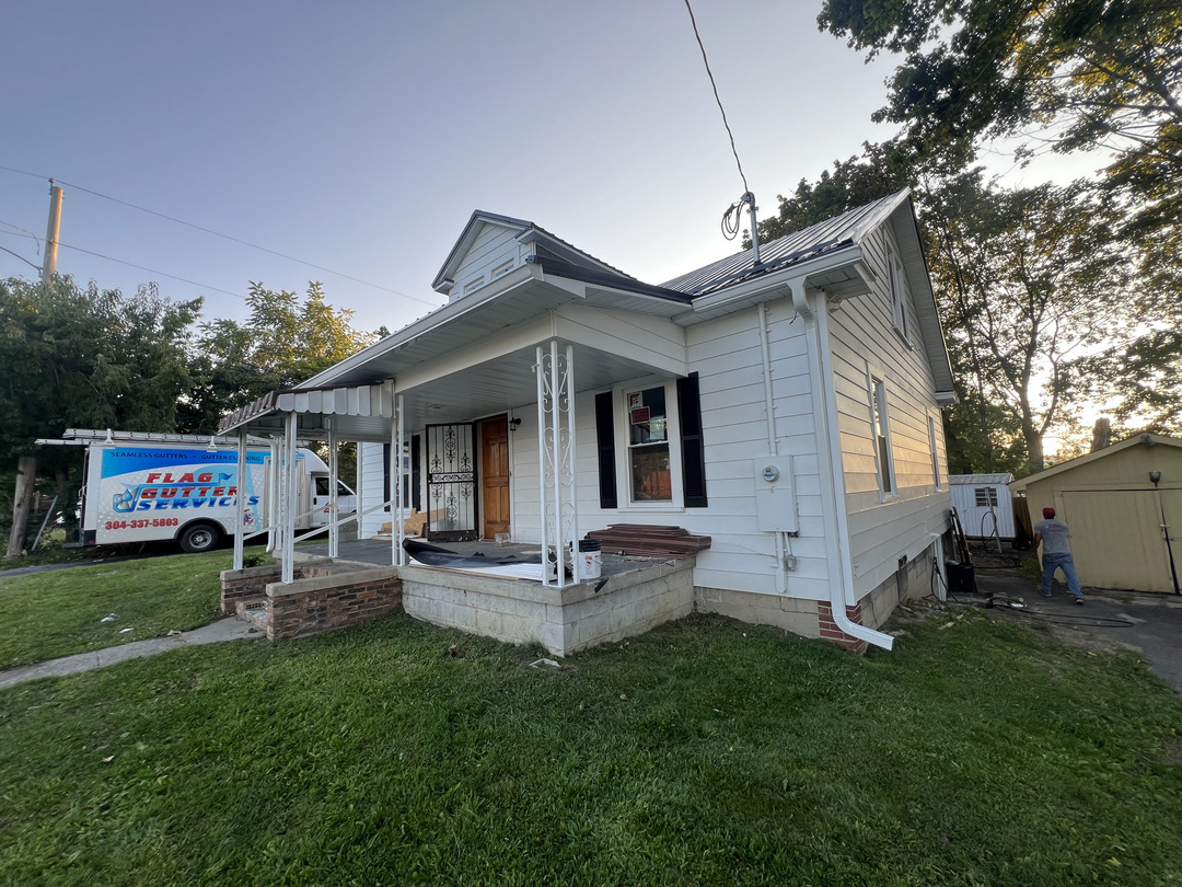 flag gutter services working on a white house with a truck parked nearby showing their branding and contact information