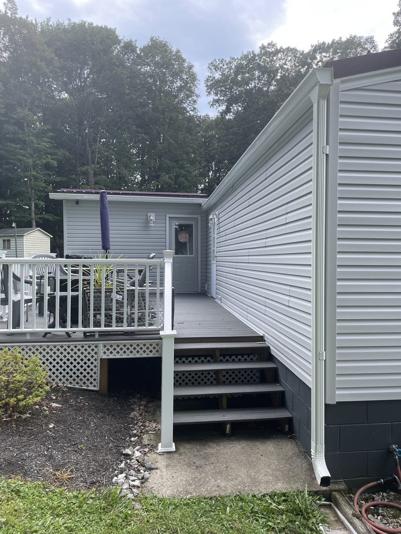 gutter installation on a house with gray siding and a wooden deck with steps leading to a door